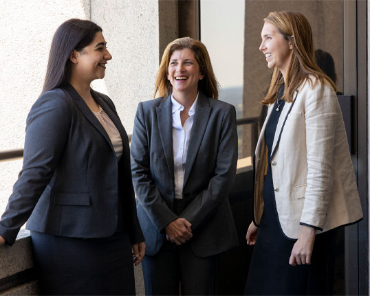 Three professional women in business attire standing together.